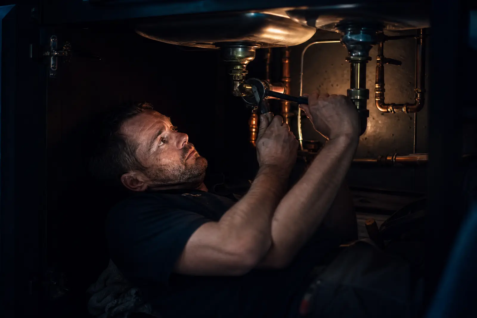 A plumber working copper supply lines under a sink.